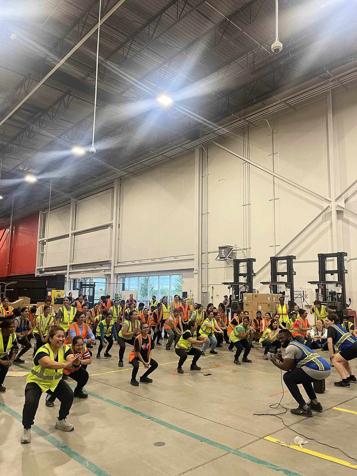 Doug on a microphone leading a large group of employees through squats at their workplace.